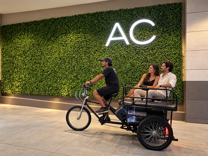 Pedicab driver carrying a couple past the green-wall entrance of the AC Hotel