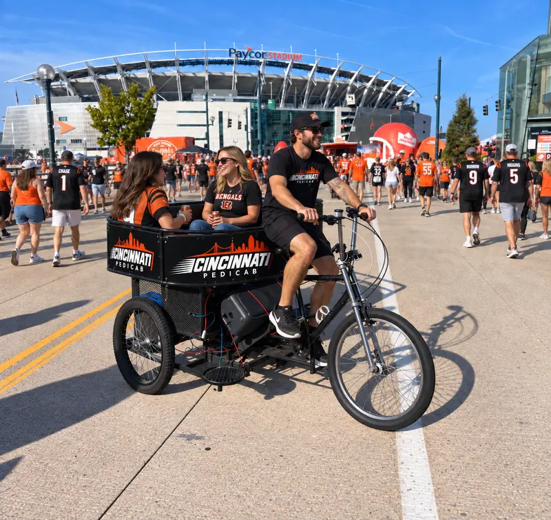 Cincinnati Pedicab driver carrying two Bengals fans through the game-day crowd outside Paycor Stadium