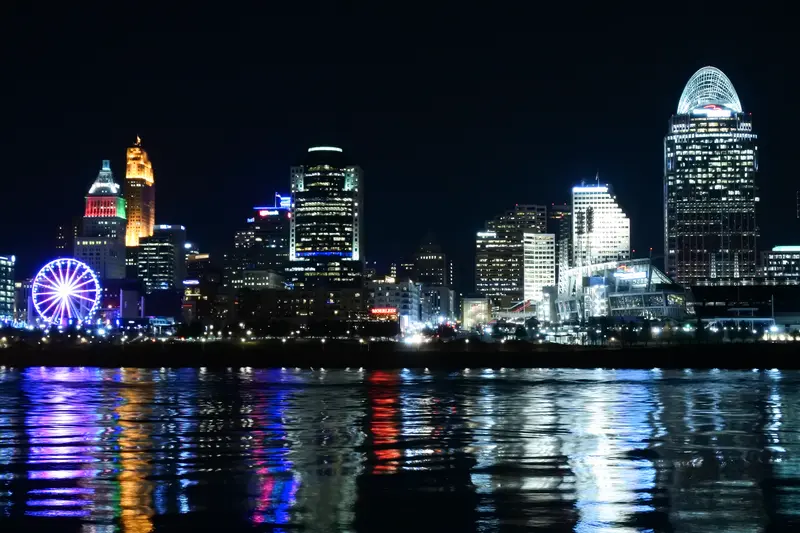 Downtown Cincinnati skyline lit up at night, reflected in the Ohio River