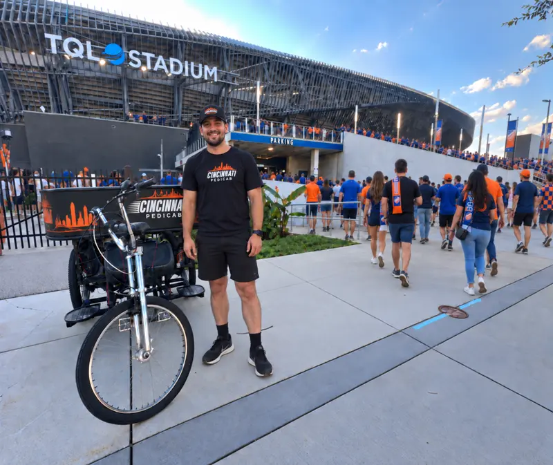 Cincinnati Pedicab driver beside a branded pedicab outside TQL Stadium on an FC Cincinnati match day
