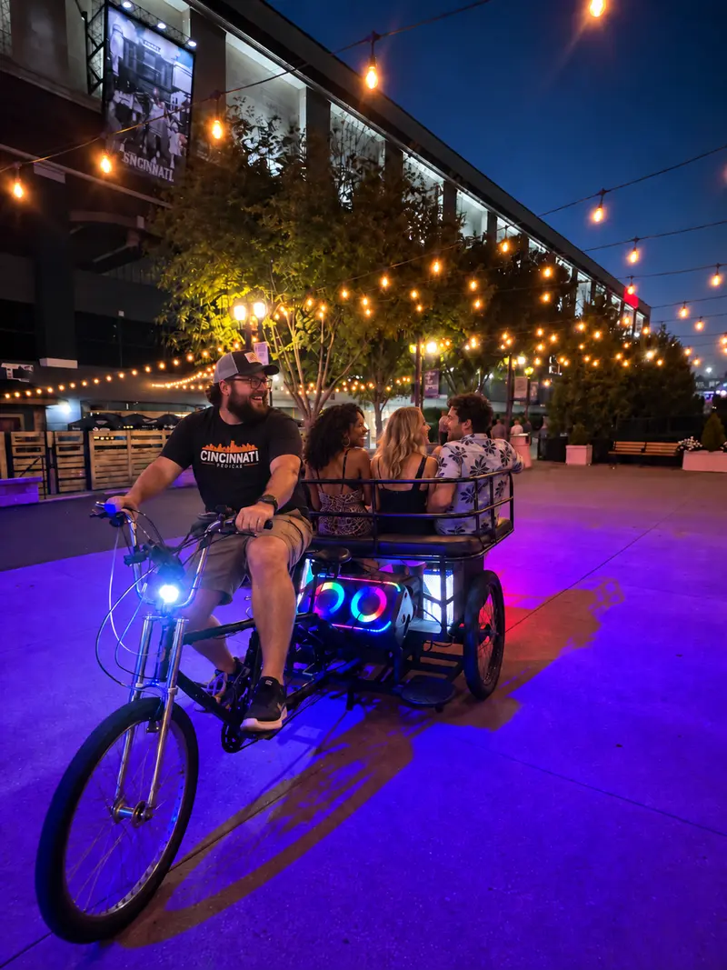 Illuminated pedicab carrying riders under string lights on a Newport plaza at night