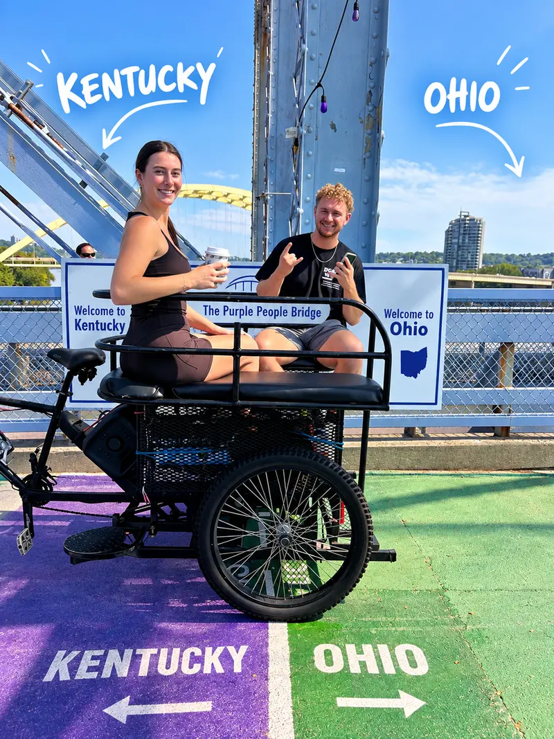 Two riders in a pedicab on the Purple People Bridge, parked right on the Kentucky–Ohio state line