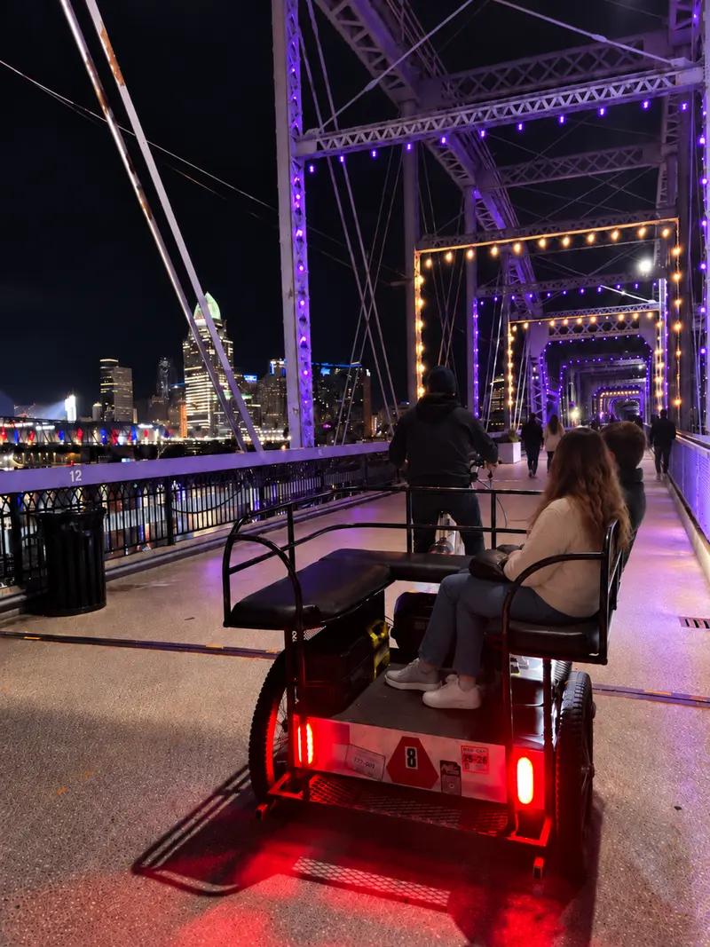 Rider in a pedicab crossing the lit-up Purple People Bridge at night